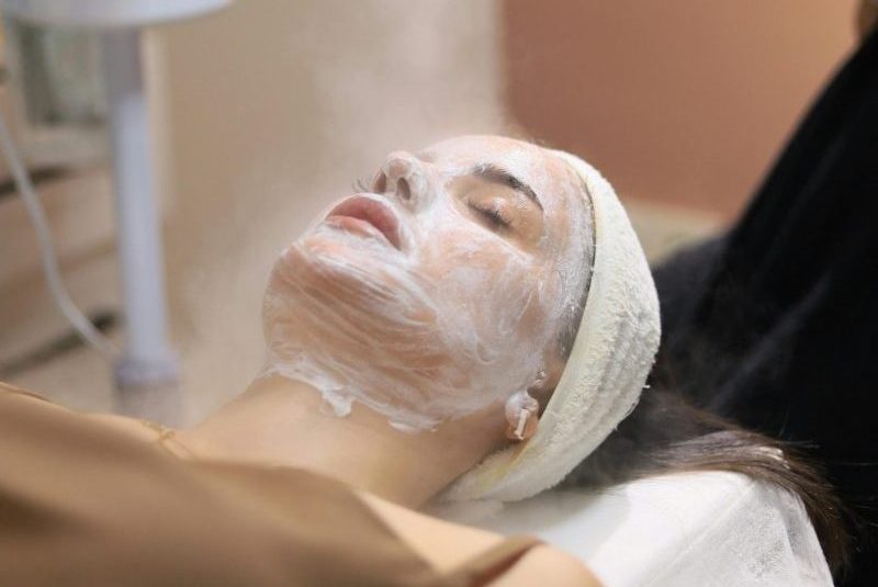 Woman enjoying a facial steam treatment in a serene spa setting.