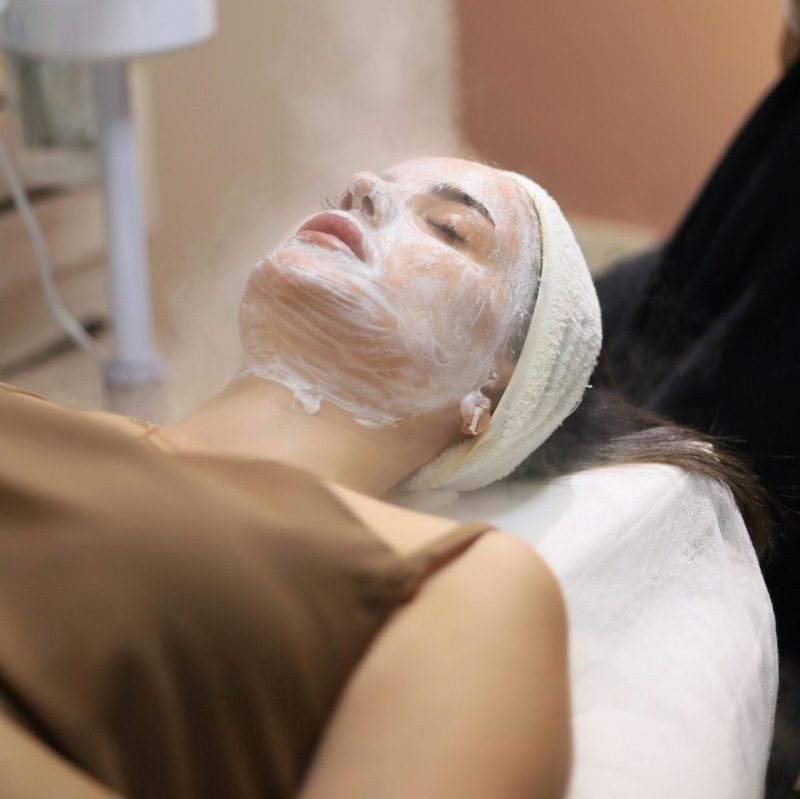 Woman enjoying a facial steam treatment in a serene spa setting.